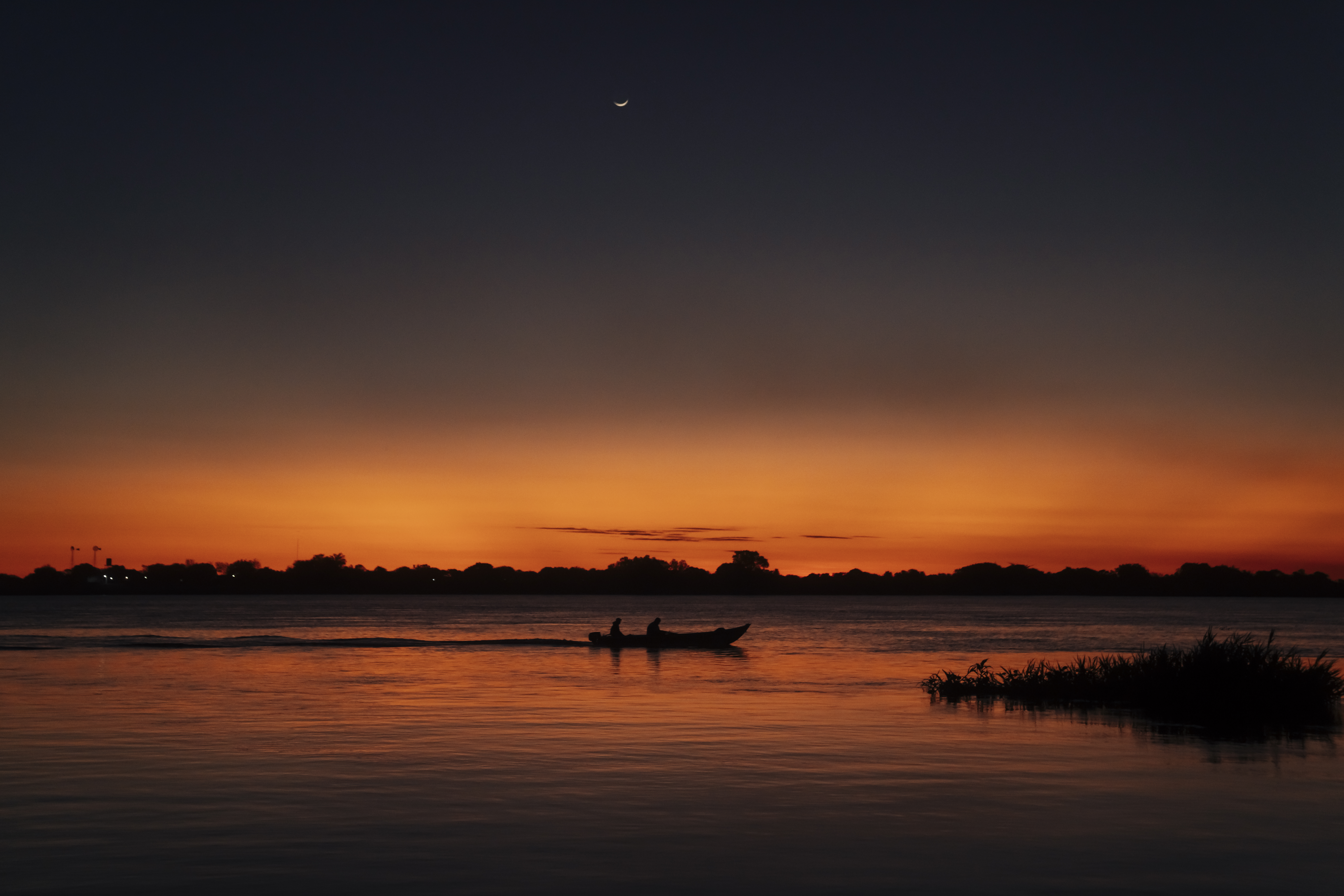 La noche cayendo con detalles de la luna, río y silueta de canoa